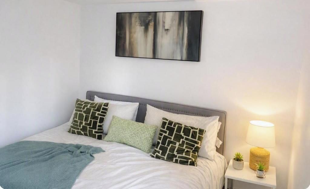 Cama bem arrumada com almofadas estampadas, abajur e uma pequena planta em uma mesa de cabeceira.