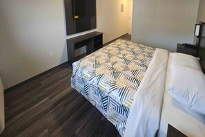 A hotel room with a bed, a TV mounted on the wall, and a dark wooden floor. - 1 King Bed | Non-Smoking (East Windsor)