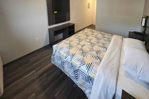 A hotel room with a bed, a TV mounted on the wall, and a dark wooden floor. - Cozy King Bed|Free Parking & Wifi (East Windsor)