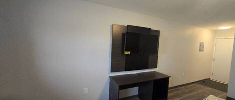 A room with a dark wooden desk, a mounted flat-screen TV, and a patterned rug.