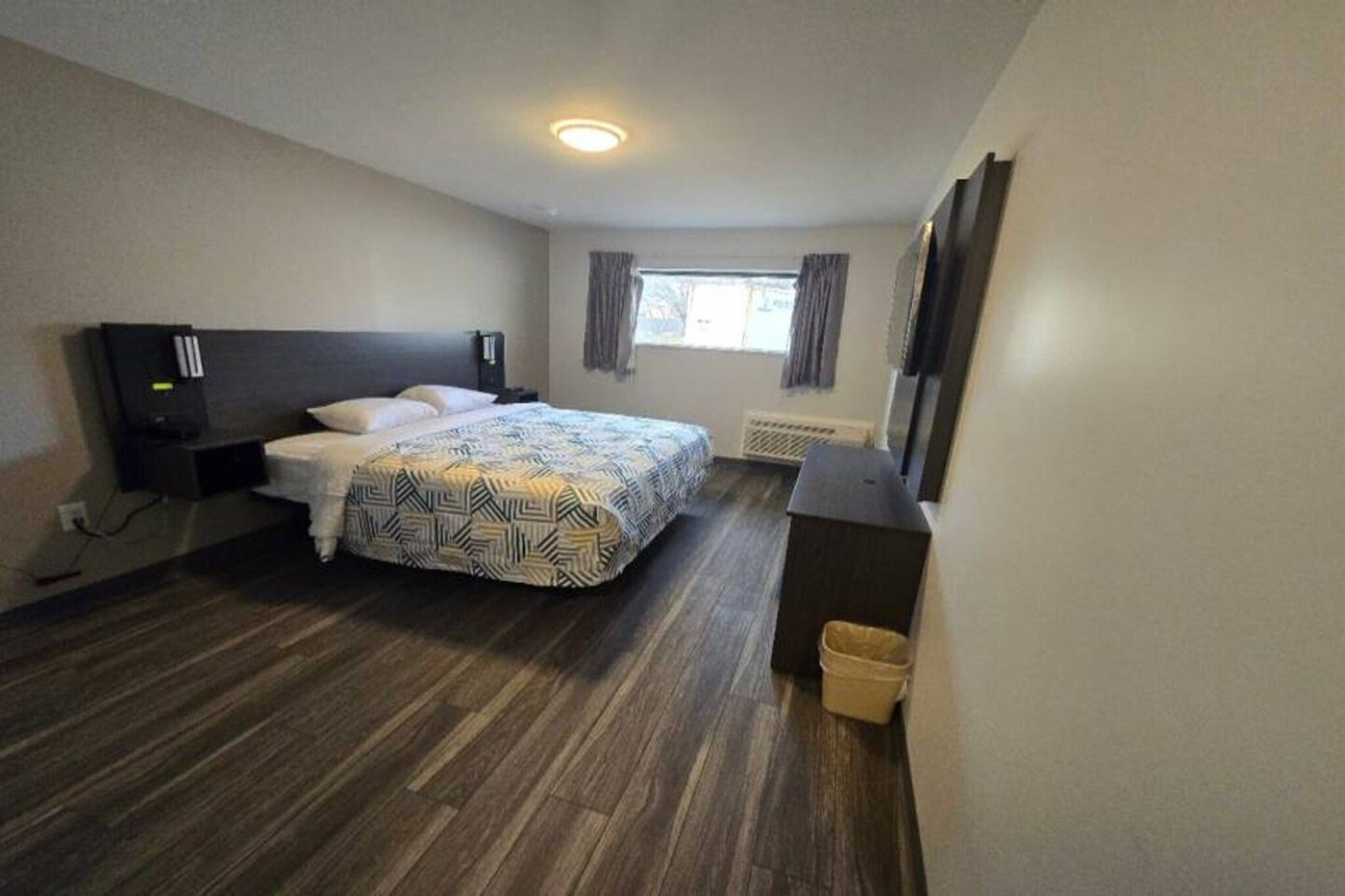 Une chambre d’hôtel avec un lit, un bureau, une télévision et une fenêtre avec des rideaux.