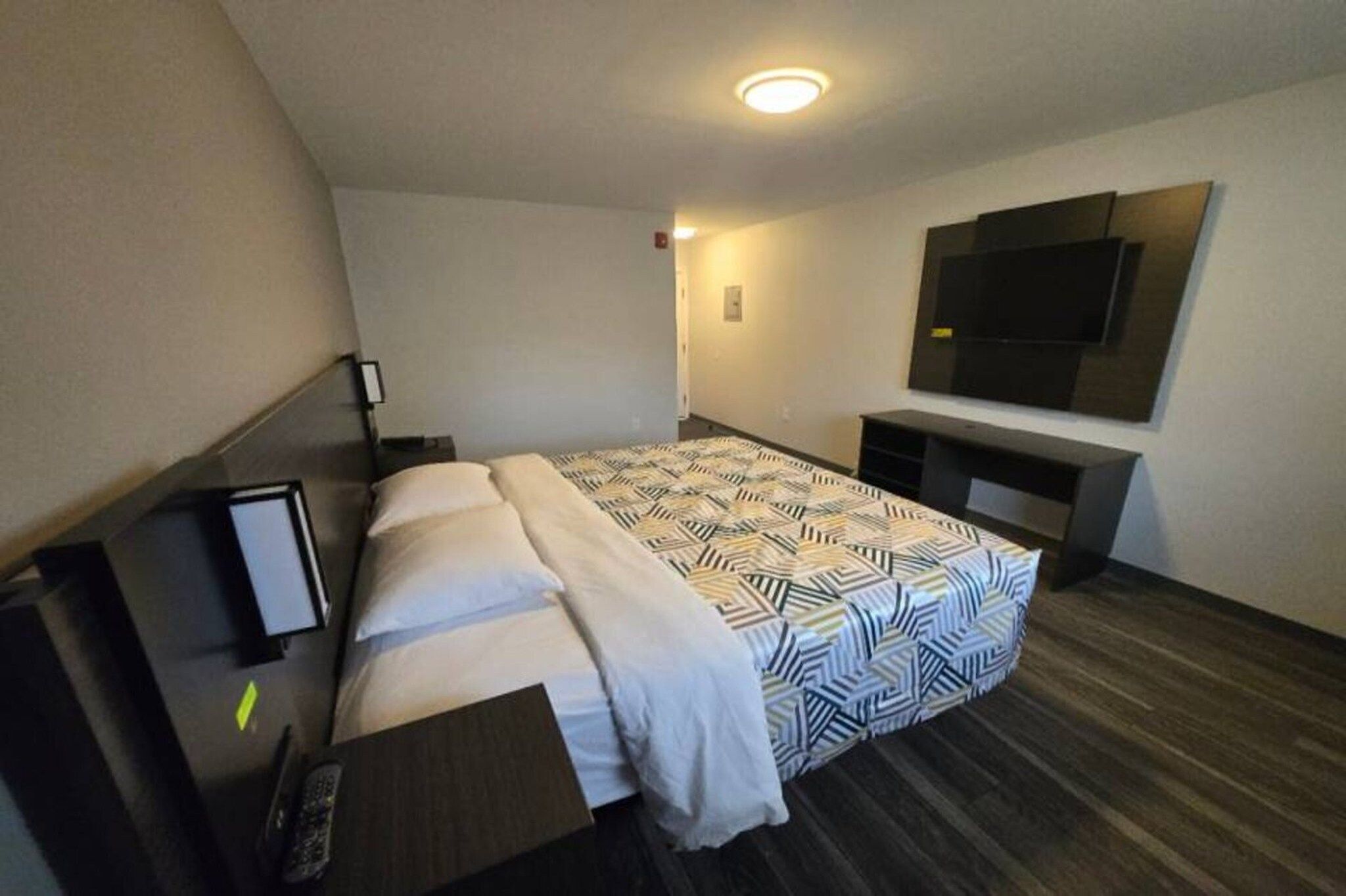 Ett hotellrum med en säng, ett skrivbord, en platt-TV och en TV som är monterad på väggen.