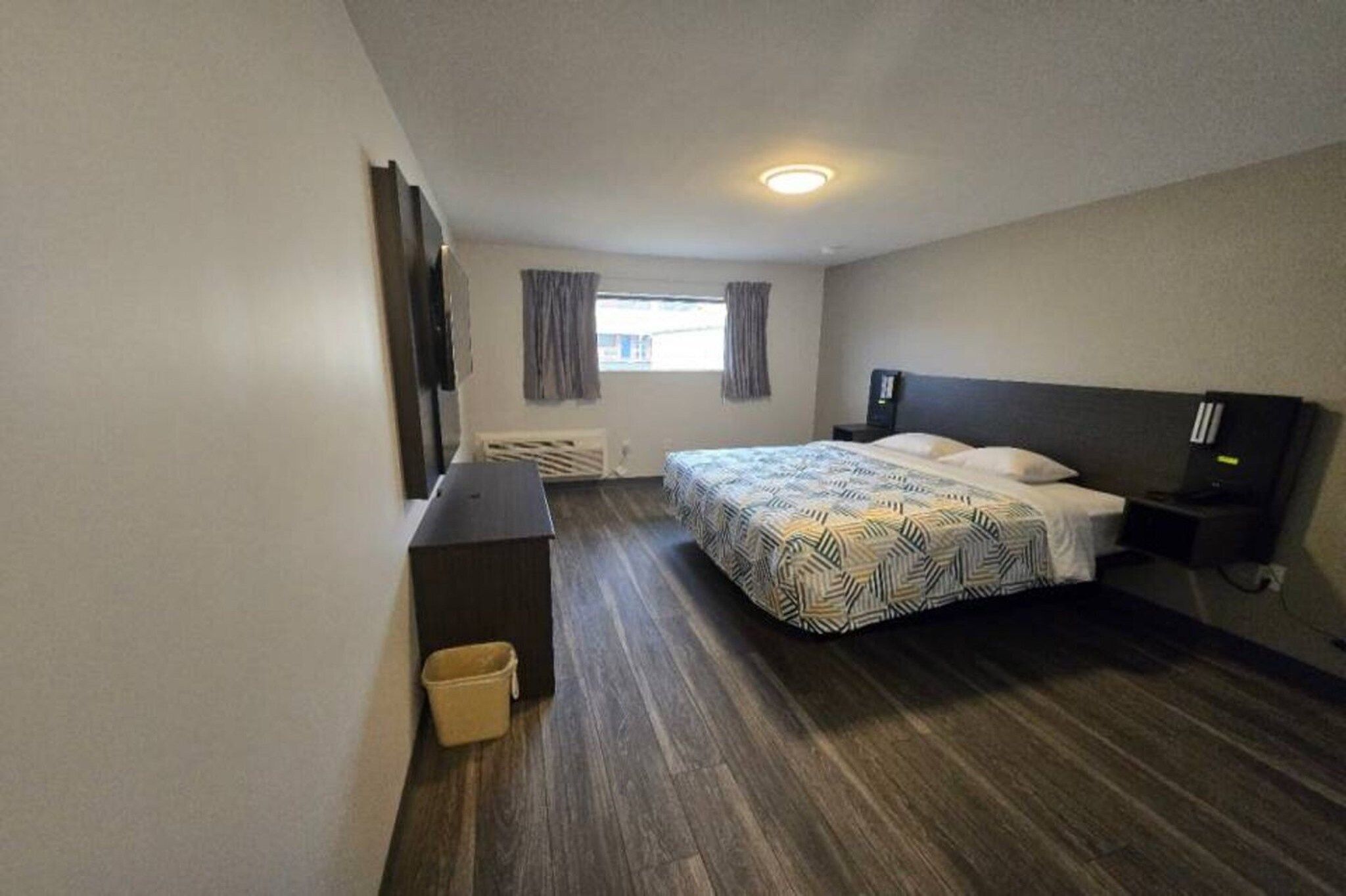 Una camera d'albergo con un letto, un comodino, una lampada e una piccola finestra.