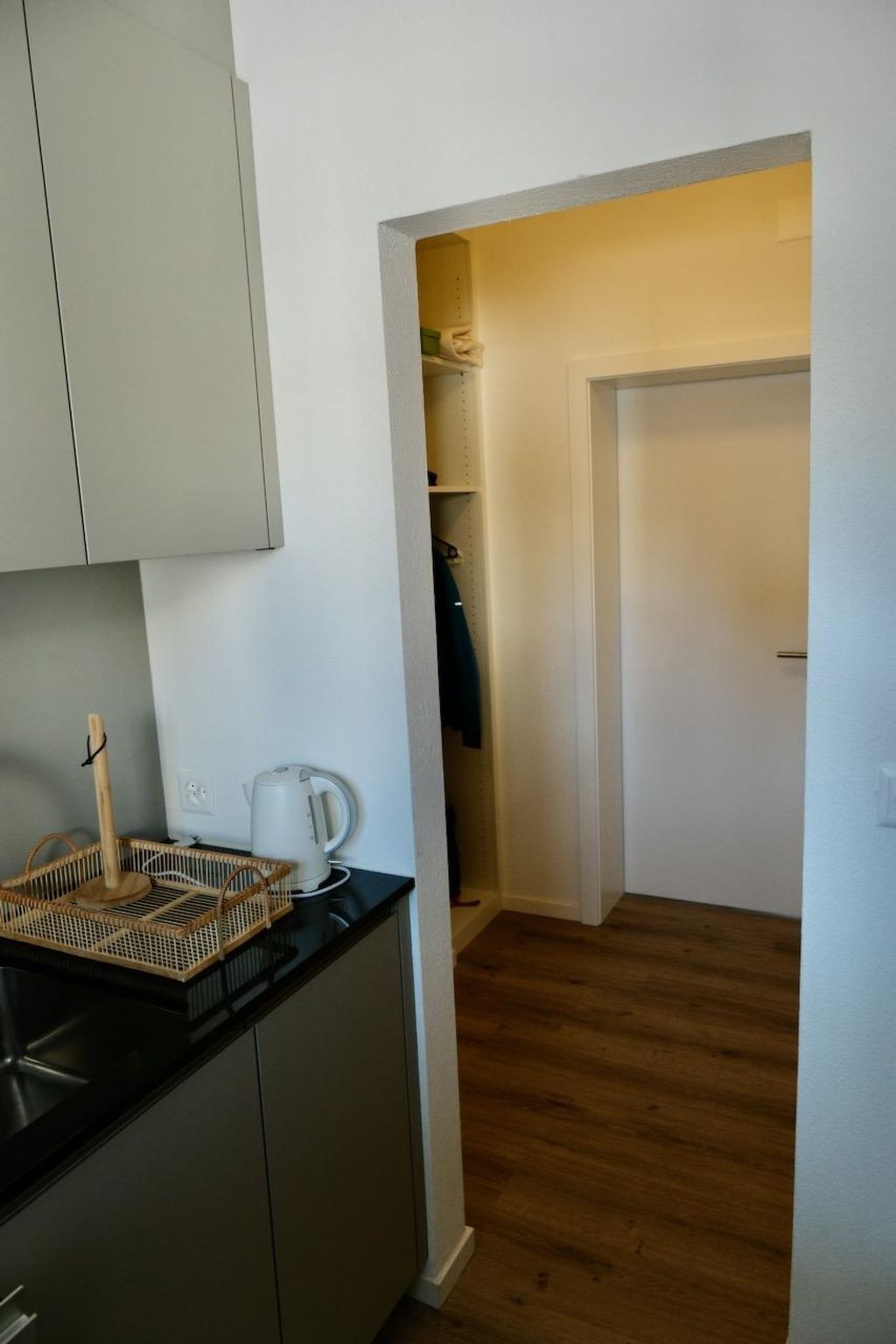 A compact kitchen with a kettle, a basket, and a wooden floor.