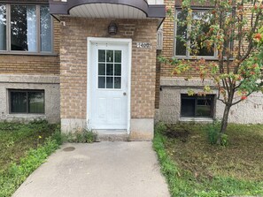 A brick building with a white door, numbered 1400, and a small tree with red flowers. - Cosy logement pour séjour confortable (Québec City)