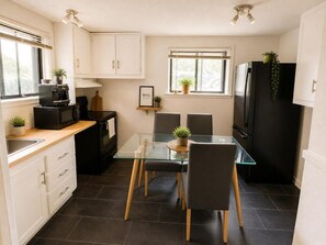 A compact kitchen with a glass dining table, two chairs, a black refrigerator, and a microwave. - Cosy logement pour séjour confortable (Québec City)