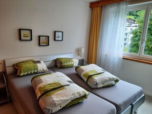 Une chambre d’hôtel avec deux lits, une fenêtre avec des rideaux et trois tableaux encadrés accrochés au mur.
