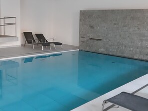 Une piscine à l’eau d’un bleu limpide, entourée d’une terrasse carrelée et d’un mur en béton.