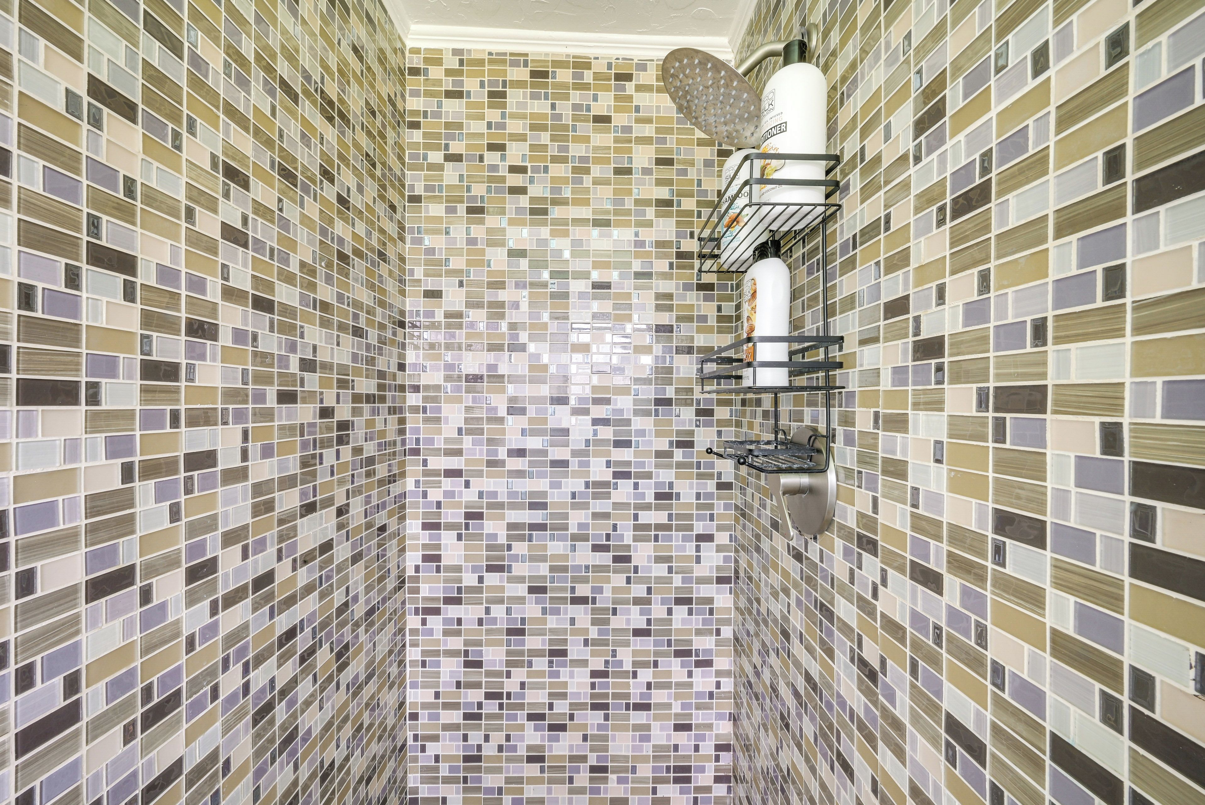 A bathroom with a tiled floor and walls, a shower area with a showerhead, and a towel rack.
