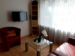 A living room with a red sofa, a glass coffee table with a plant, a TV mounted on the wall, and a wooden bookshelf. - Quellenhof C04 Appartement/Fewo, Dusche oder Bad, WC 2-Zimmerwohnung by Interhome (Davos)