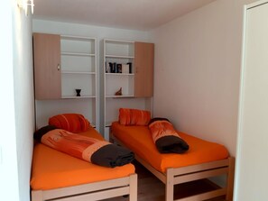 A room with two beds, each with orange bedding and pillows, and a white wall with a shelf above. - Quellenhof C04 Appartement/Fewo, Dusche oder Bad, WC 2-Zimmerwohnung by Interhome (Davos)