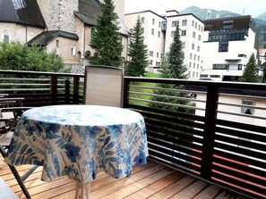 A balcony with a table covered by a floral tablecloth, a wooden deck, and a view of buildings and trees. - Quellenhof C04 Appartement/Fewo, Dusche oder Bad, WC 2-Zimmerwohnung by Interhome (Davos)