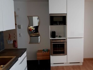 A kitchen with white cabinets, a built-in oven, a microwave, and a refrigerator. - Quellenhof C04 Appartement/Fewo, Dusche oder Bad, WC 2-Zimmerwohnung by Interhome (Davos)