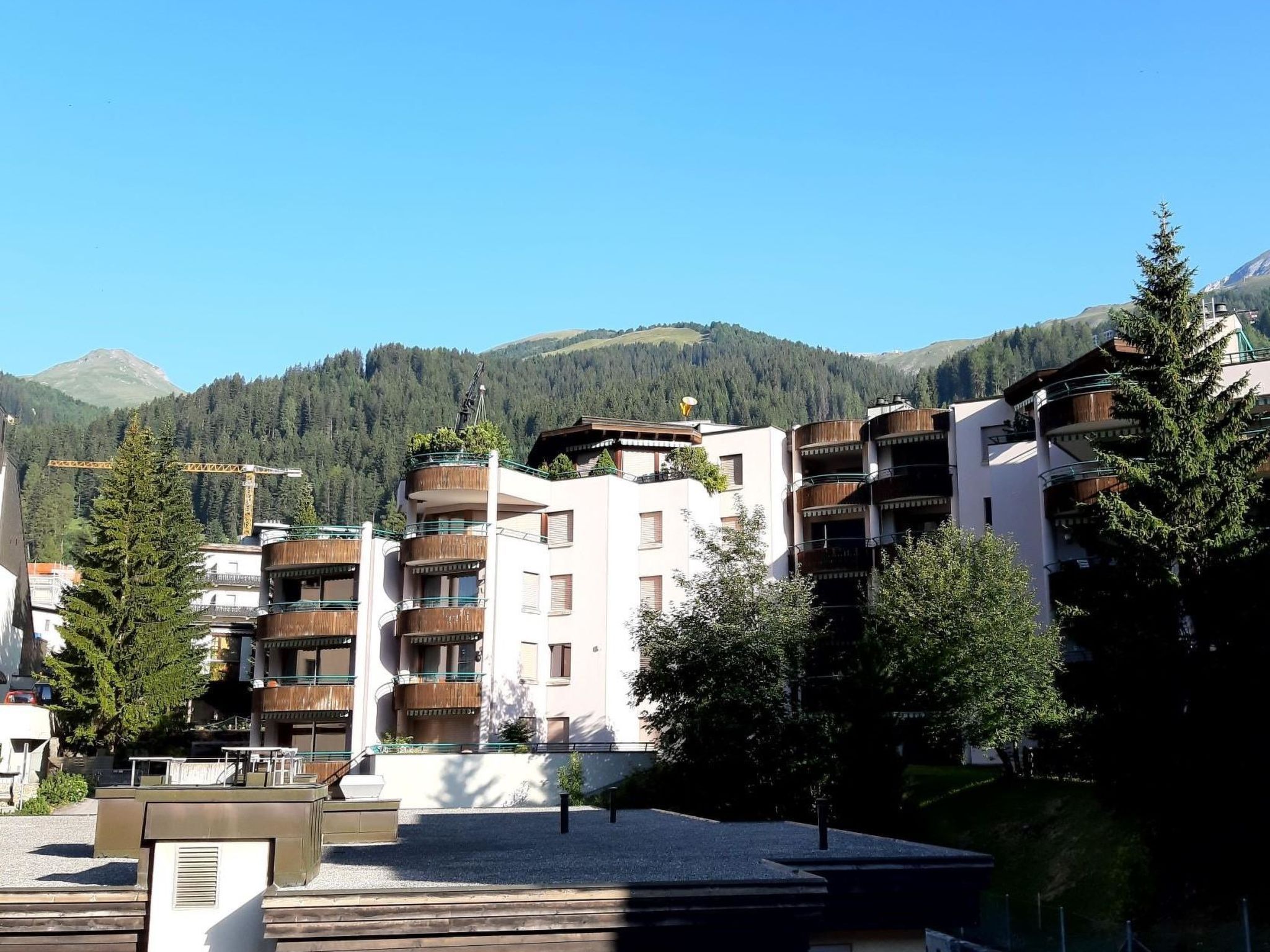 Un edificio de varios pisos con balcones, rodeado de árboles y un paisaje montañoso.