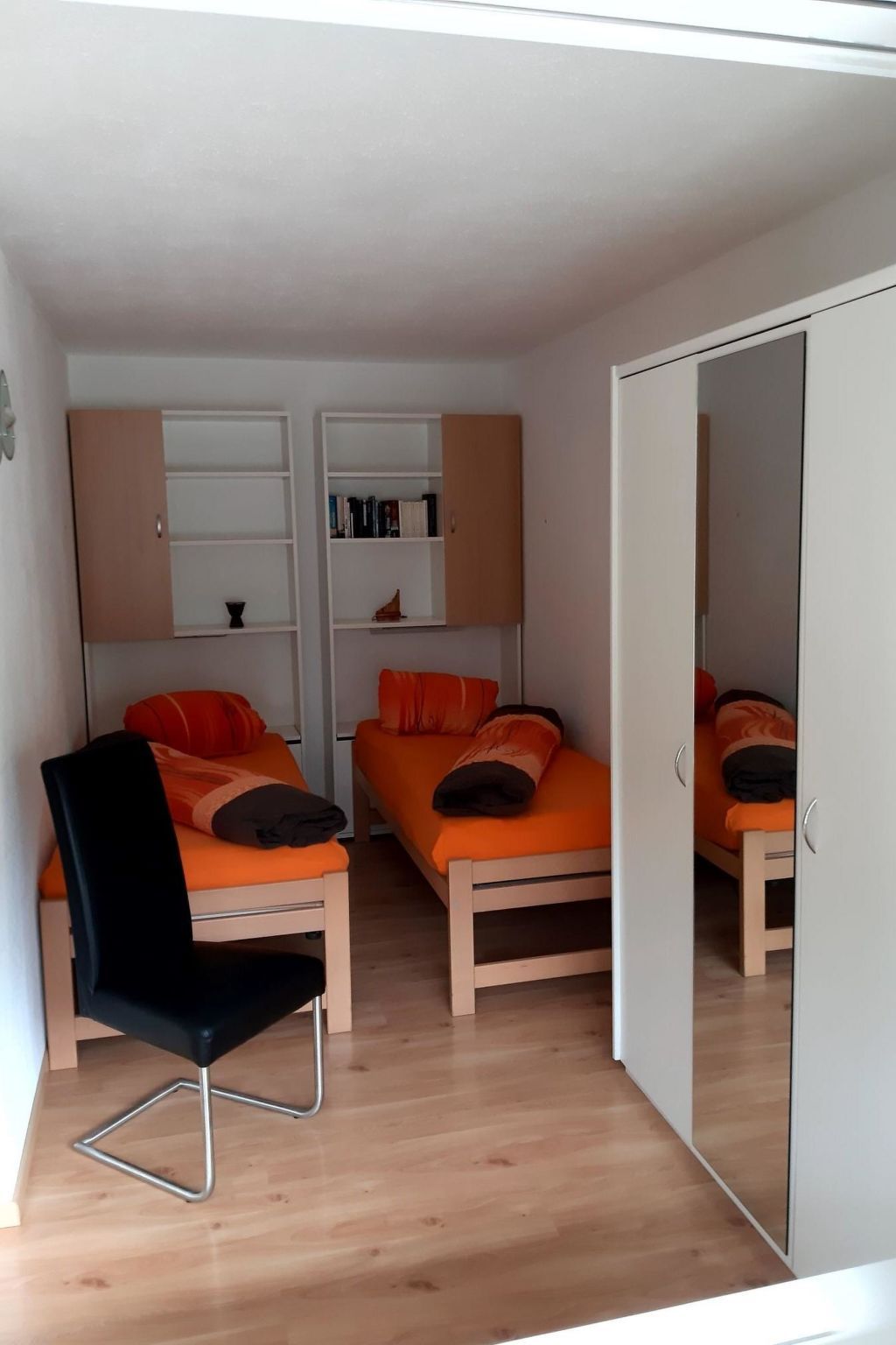 A compact bedroom with two beds, a chair, and a wardrobe.
