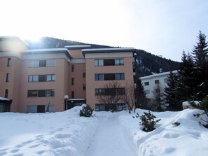 Un immeuble à plusieurs étages, dont le sol est recouvert de neige, avec une montagne en arrière-plan.
