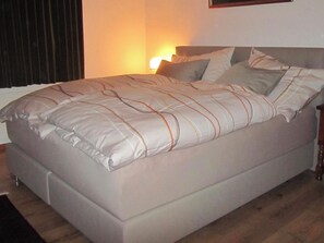 A bed with a white and orange striped blanket, a wooden headboard, and a bedside lamp. - Carlton am Golf C46 Appartement/Fewo, Dusche oder Bad, WC 2-Zimmerwohnung by Interhome (Davos)