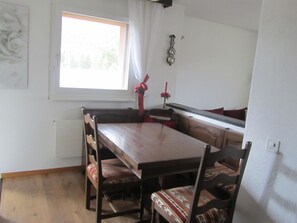 A dining area with a wooden table and chairs, a window with curtains, a wall clock, and a small plant. - Carlton am Golf C46 Appartement/Fewo, Dusche oder Bad, WC 2-Zimmerwohnung by Interhome (Davos)