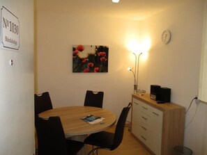 Un coin repas comprenant une table ronde, quatre chaises, un tableau, une horloge et une lampe.