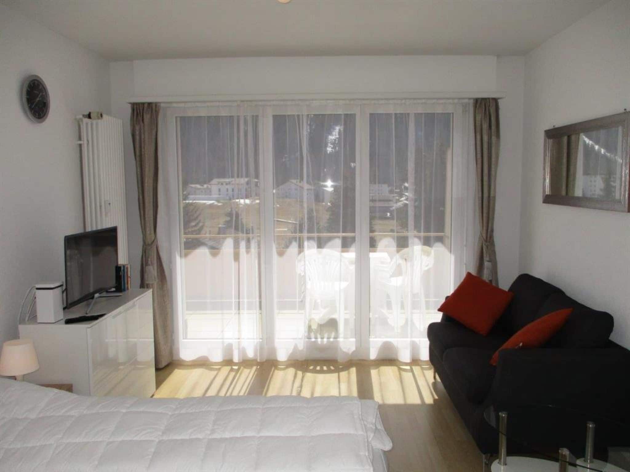 Une chambre d’hôtel avec un lit, une télévision, un canapé et une grande fenêtre avec des rideaux.