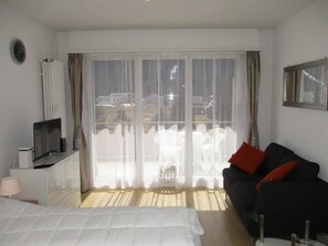 Une chambre d’hôtel avec un lit, une télévision, un canapé et une grande fenêtre avec des rideaux.