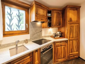A kitchen with wooden cabinets, a built-in oven, and a window with a tree design. - Bündastrasse 22 EG Appartement/Fewo, Dusche oder Bad, WC 2 1/2-Zimmerwohnung by Interhome (Davos)