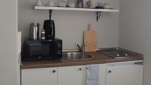 Eine kleine Küche mit weißen Schränken, einer Holzausziehtafel, einer Kaffeemaschine, einem Toaster, einem Spülbecken und einem Handtuch.