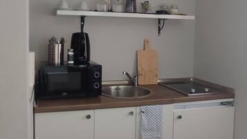 Ett kompakt kök med vita skåp, en bänkskiva i trä, en kaffebryggare, en brödrost, ett handfat och en handduk som hänger på en krok.
