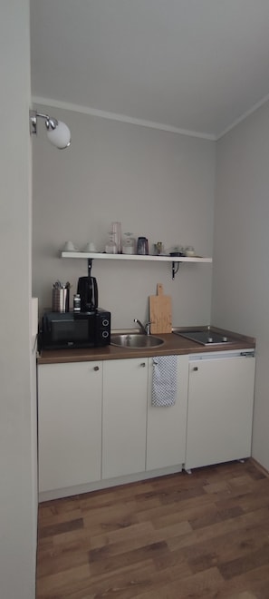 Ett kompakt kök med vita skåp, en bänkskiva i trä, en kaffebryggare, en brödrost, ett handfat och en handduk som hänger på en krok.