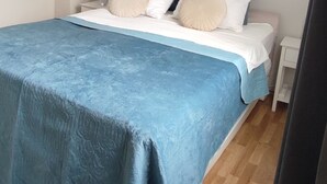 Ein Schlafzimmer mit Bett, Kissen, einem Nachttisch, einem gerahmten Bild an der Wand und einem Fenster.