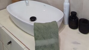 Ein Badezimmer mit rundem Spiegel, Waschbecken in Weiß, Handtuch und Pflegeprodukten.
