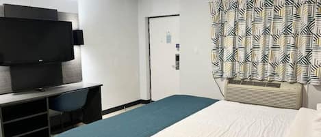 Una camera d'albergo con un letto, una scrivania con TV a schermo piatto, una porta e tende a motivi.