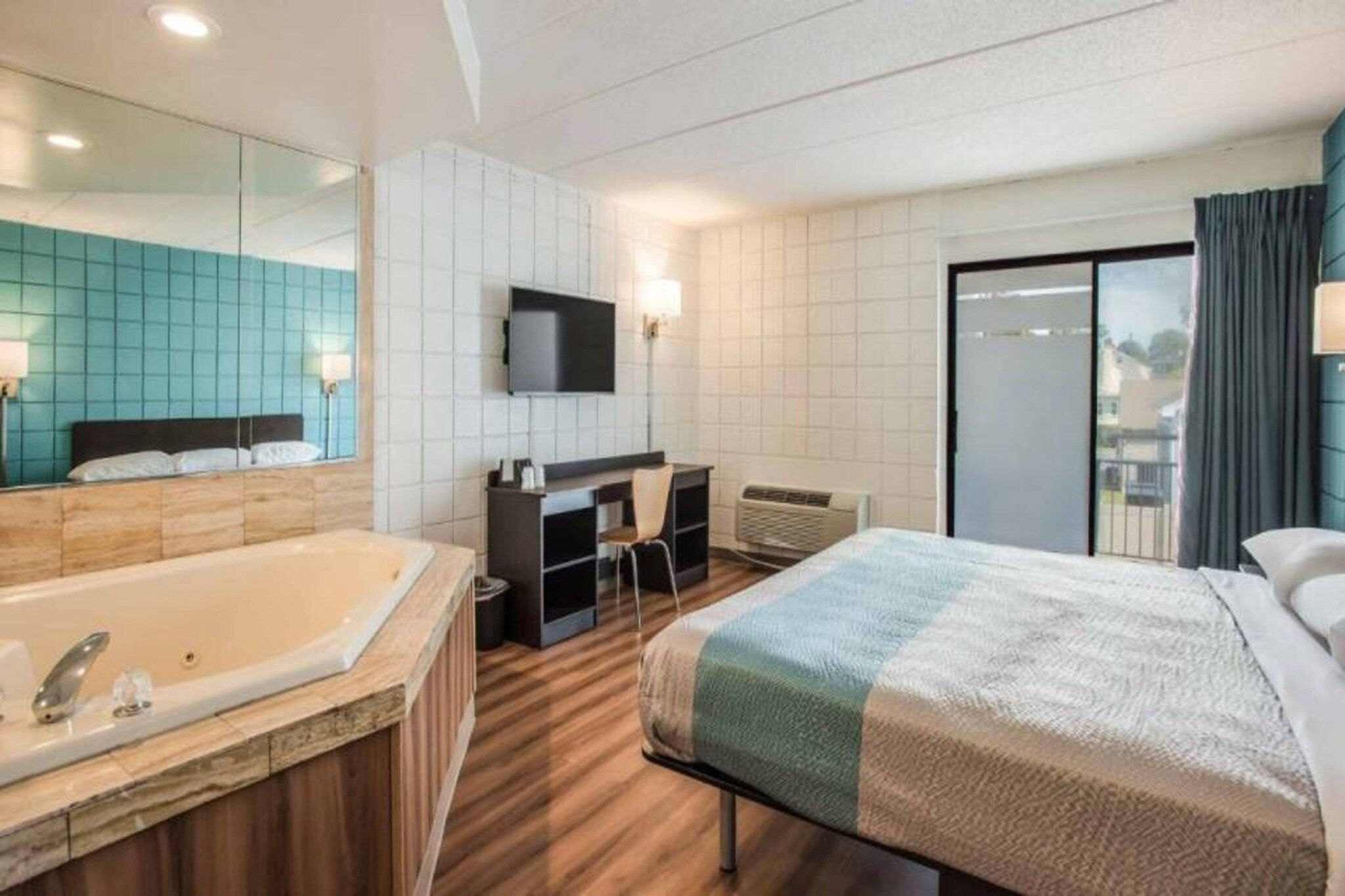 Habitación de hotel con una cama grande, baño independiente con bañera, escritorio con silla, televisor de pantalla plana montado en la pared y puerta corrediza de vidrio que da a un balcón.