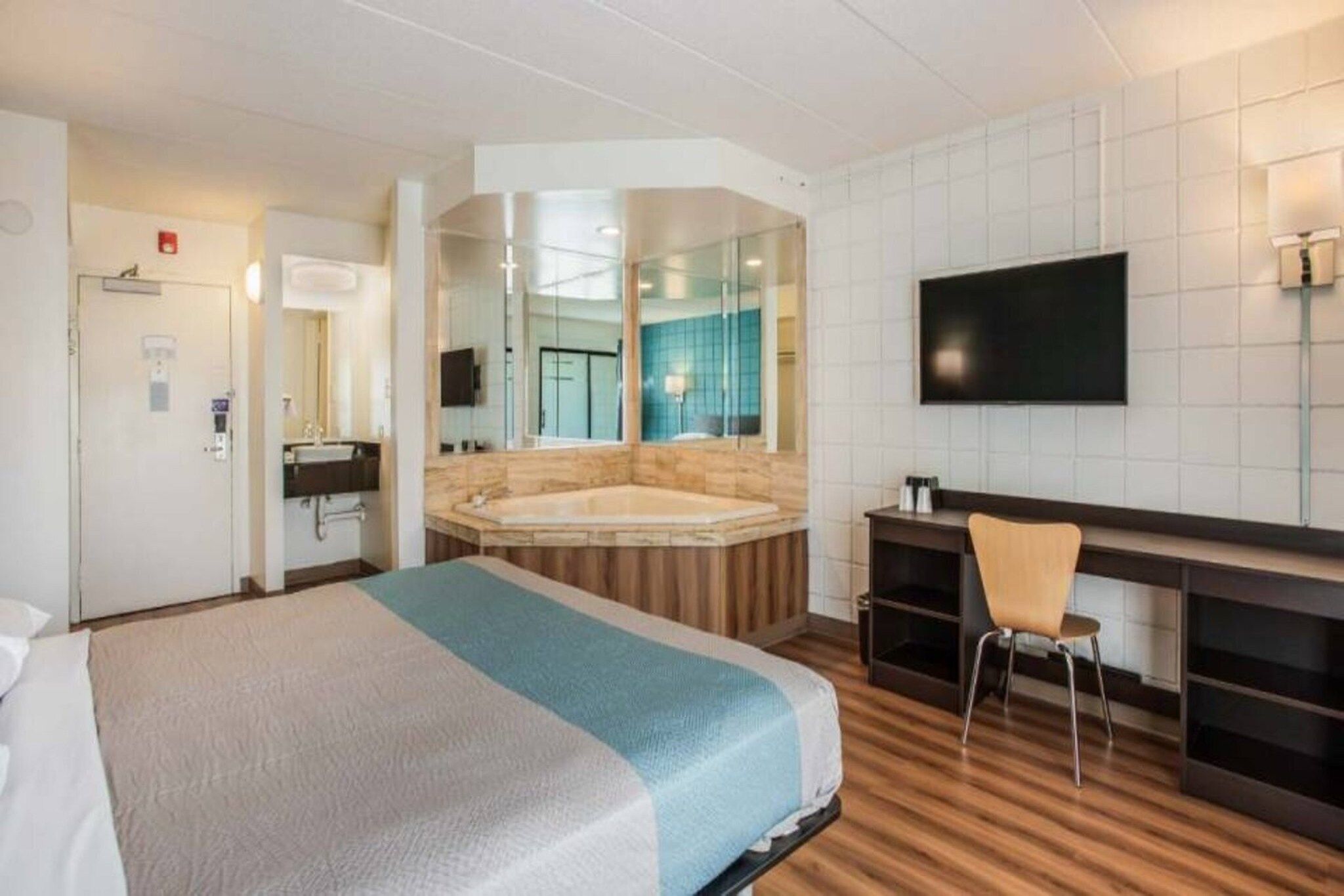 A hotel room with a large bed, a sitting area with a desk and chair, a television, and a bathroom with a bathtub and mirror.