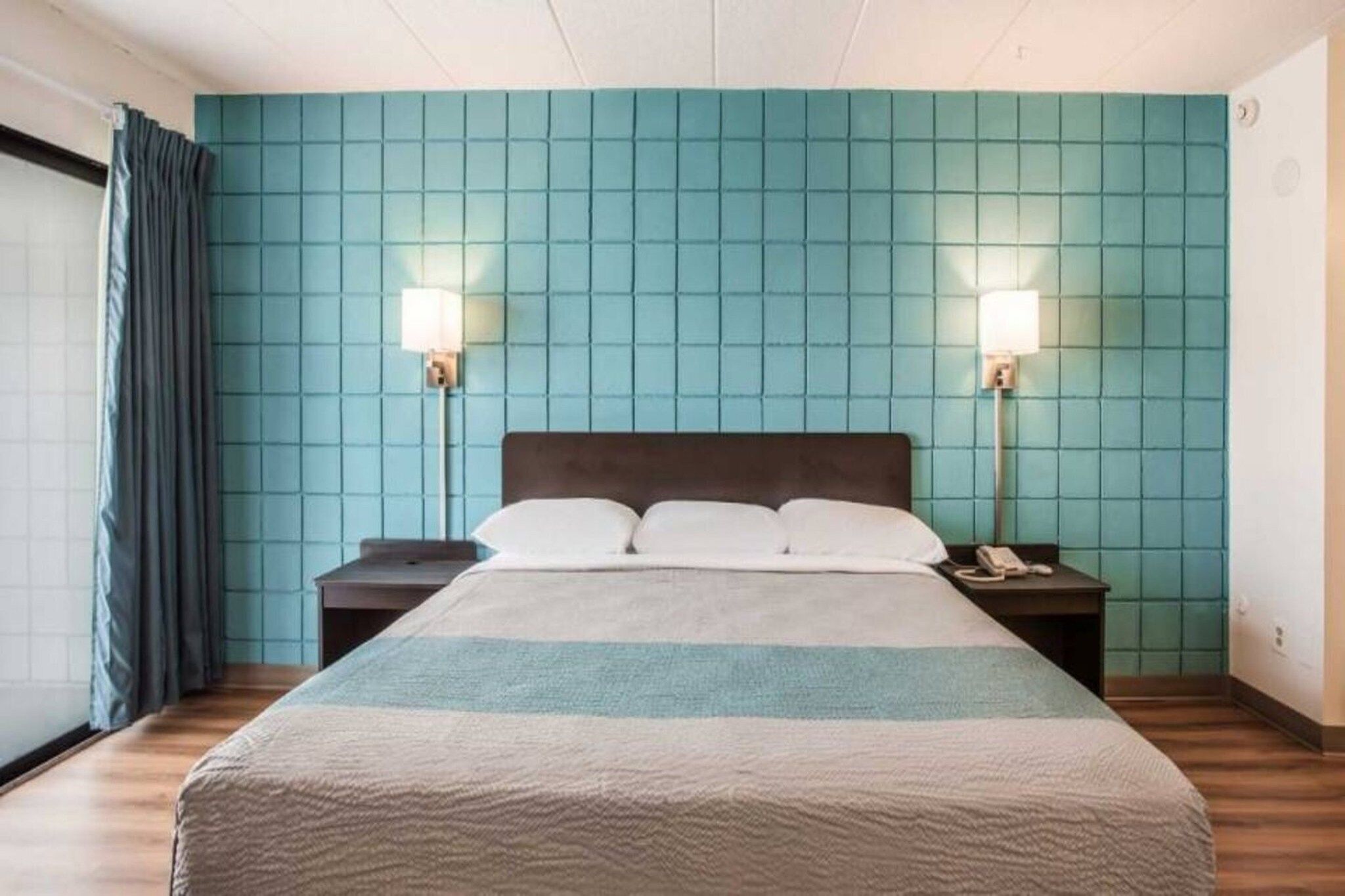 Una habitació d'hotel amb un llit gran, dues taules de nit, un telèfon i una finestra amb cortines.