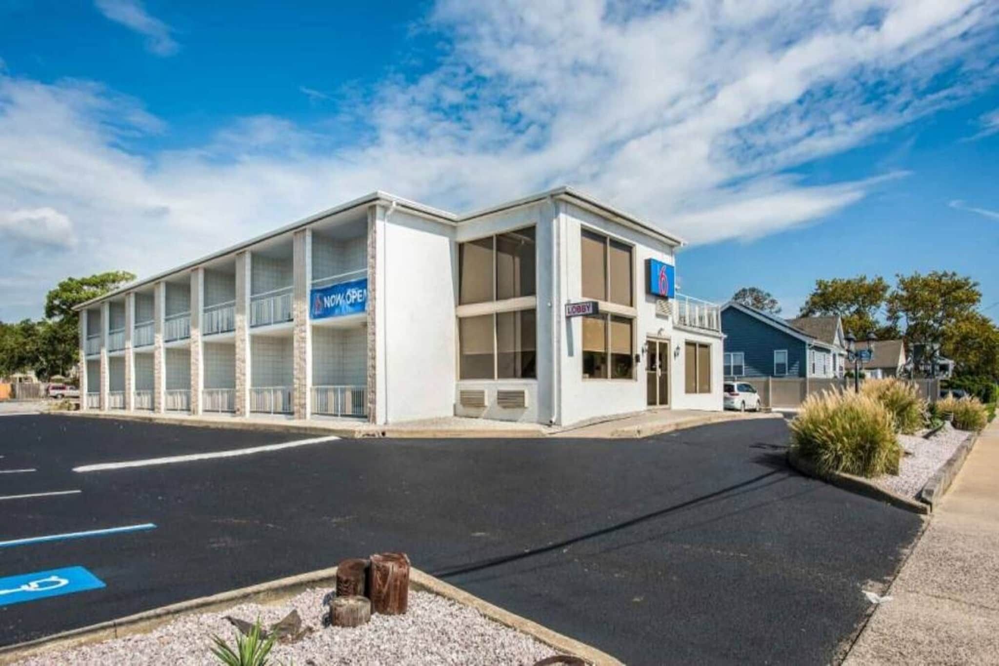 Un hotel moderno con una estructura de dos pisos, un vestíbulo visible y un estacionamiento con espacios delimitados.