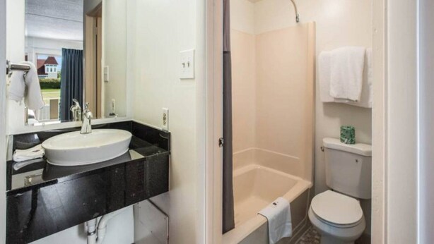 Une salle de bain avec un lavabo blanc, un plan de toilette noir et une cabine de douche.