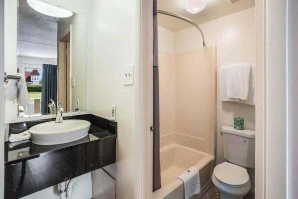 Un baño con lavamanos blanco, encimera negra y cabina de ducha.