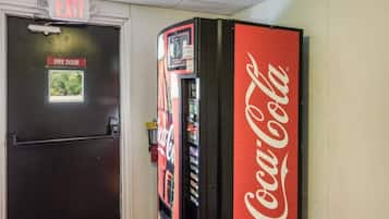 Una puerta cortafuegos con letrero de salida, una máquina expendedora de Coca-Cola y una ventana con vista a zonas verdes.