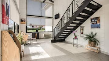Un interior espacioso con techo alto, una escalera con barandilla negra y un gran ventanal con vistas al exterior.