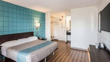 Habitación de hotel con cama, mesita de noche, lámpara y vista al baño.