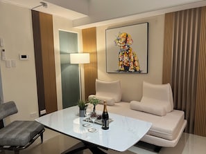 A modern living room with a white sofa, a glass coffee table, and a colorful abstract painting. - Modern Cozy Sunlit Apt Next to AirportS (ParaƱaque)