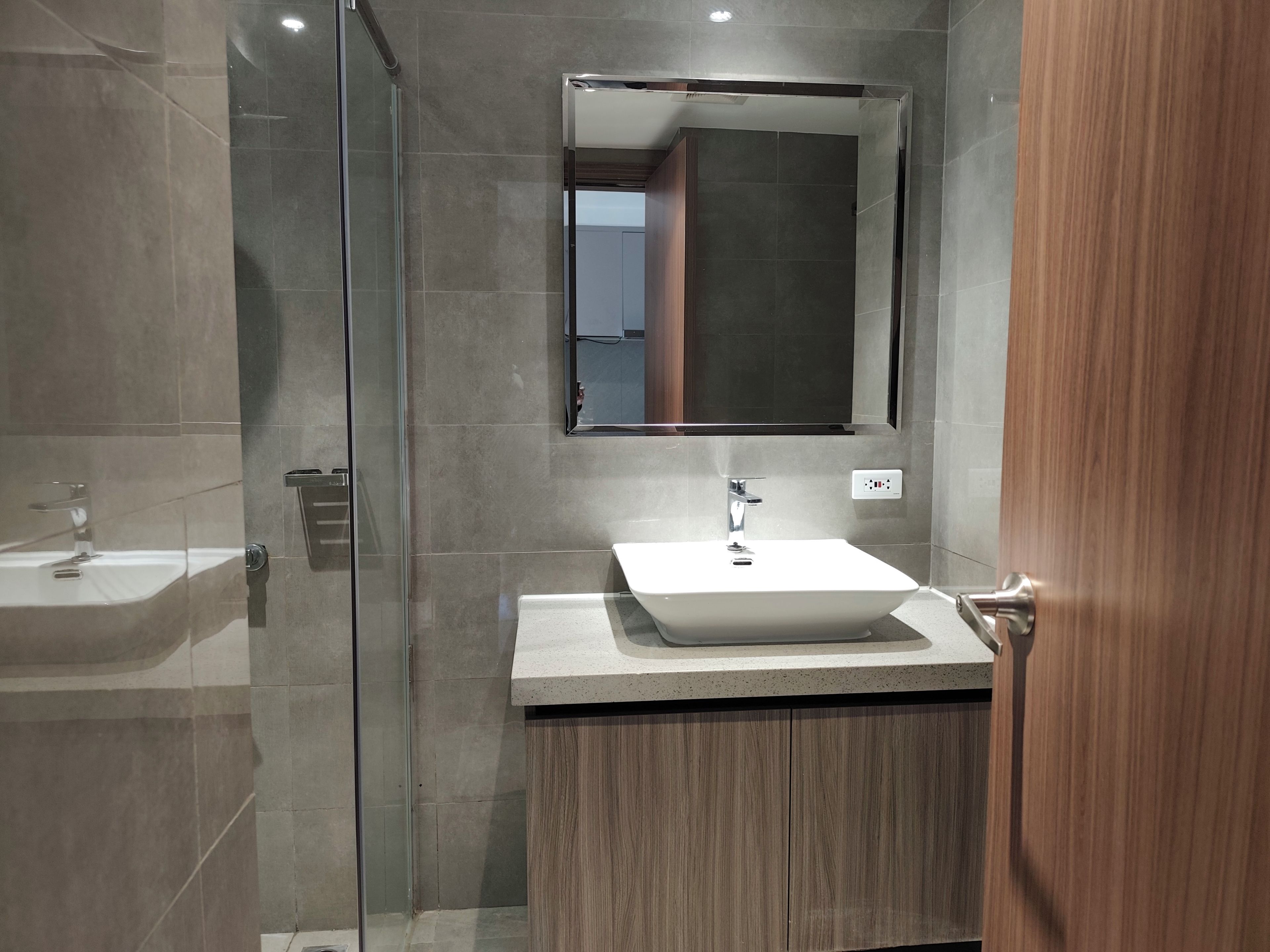 A modern bathroom with a glass shower enclosure, a white sink, and a wooden vanity.