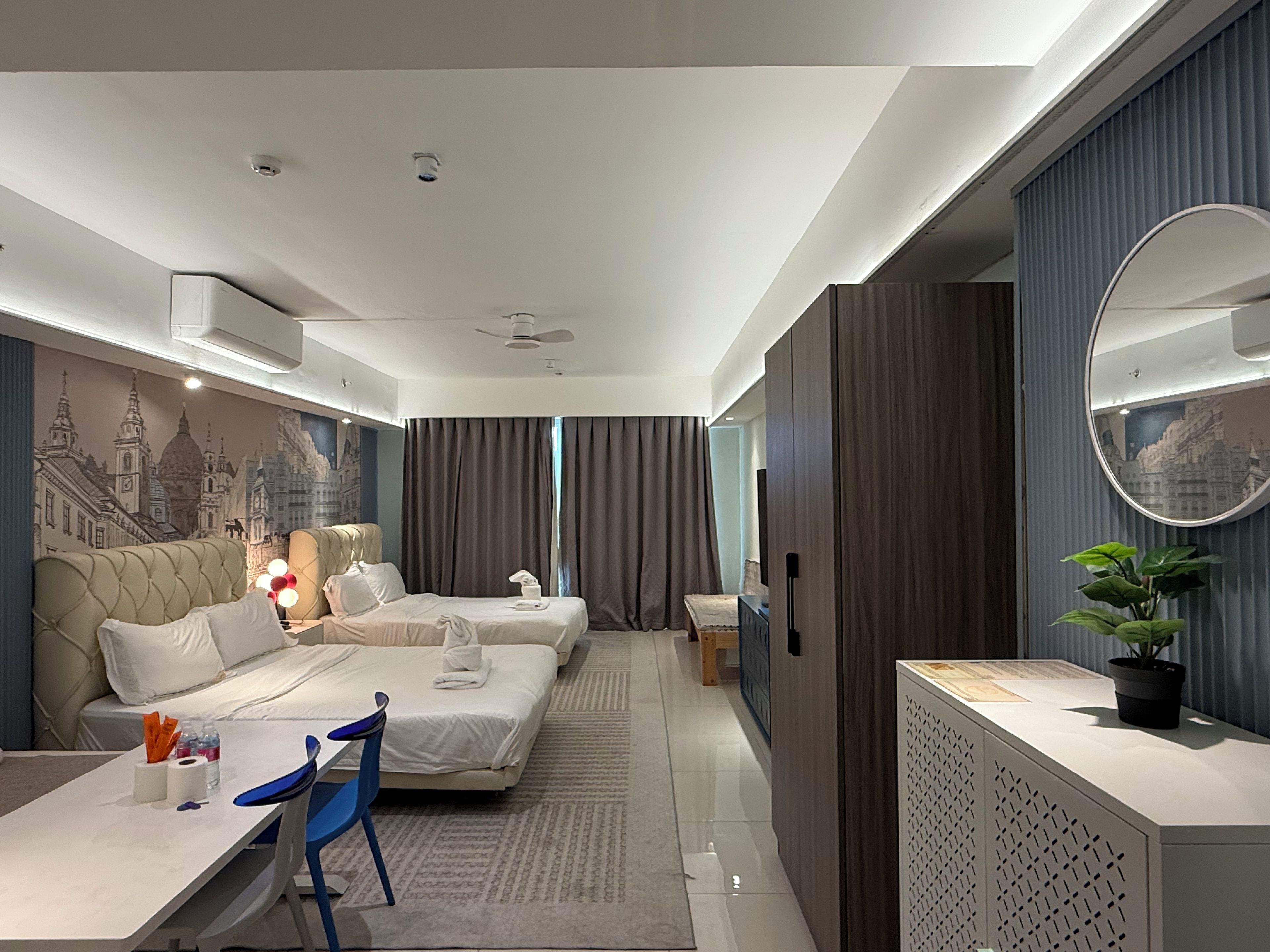 Una habitación de hotel moderna con cama, escritorio, silla, espejo y una planta.