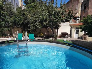 Una piscina con superficie d'acqua cristallina e blu, circondata da alberi e un edificio con tetto in tegole.