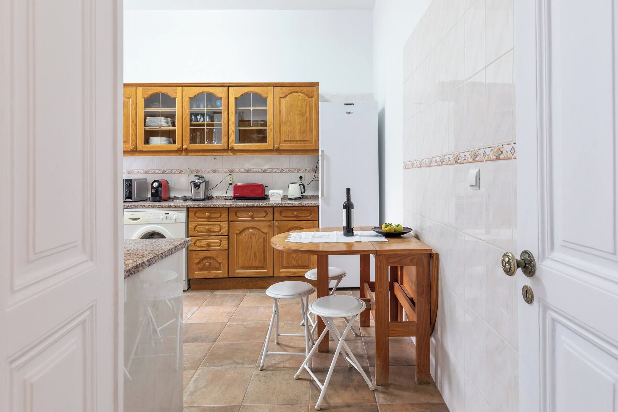 Une cuisine compacte avec des meubles en bois, un lave-linge encastré et un coin repas équipé de tabourets.