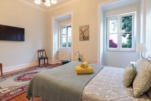 Ein Schlafzimmer mit einem Bett, einem Sessel, einem Fernseher und zwei Fenstern.