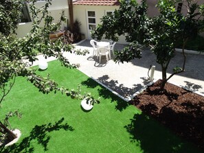 Eine Terrasse mit Kunstgrashalm, weißen Plastikstühlen und einem kleinen Tisch.