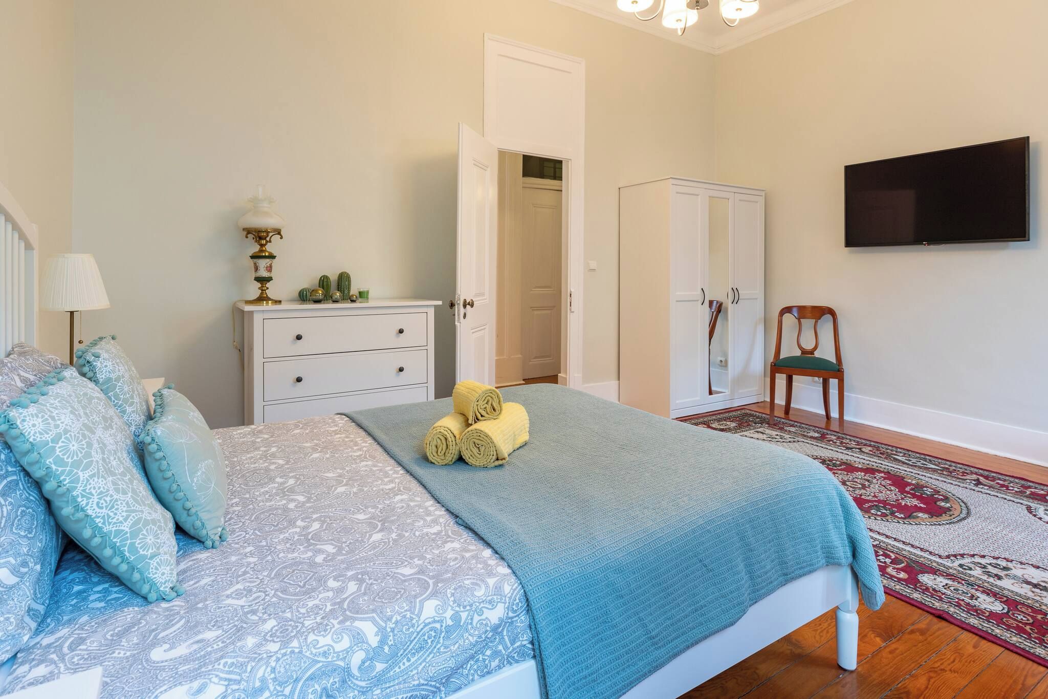 A bedroom with a bed, a dresser, a chair, a television, and a wardrobe.