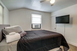 Ein Schlafzimmer mit Bett, Fenster, Deckenventilator und Fernseher an der Wand.